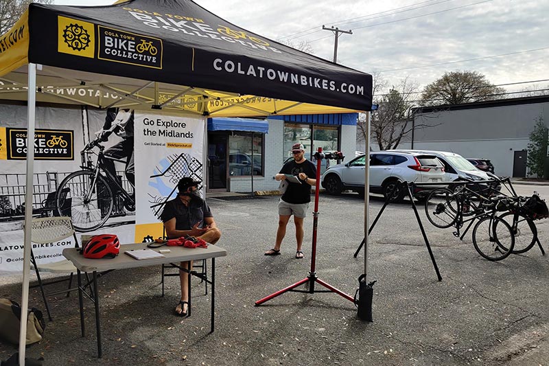 Team member accepting bikes at a bike valet under a Cola Town Bike Collective tent